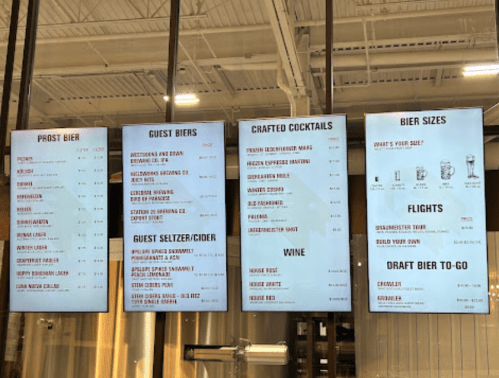 Menu board displaying various beers, cocktails, wines, and sizes available at a brewery.