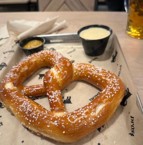 A large salted pretzel on a tray with mustard and cheese dip in black cups.