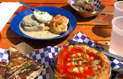 A colorful spread of comfort food including biscuits, gravy, a savory pie, and a cheesy dish on a wooden table.