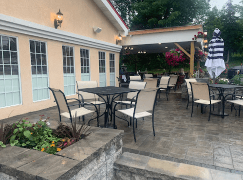 Outdoor dining area with tables and chairs, surrounded by flowers and a covered patio.