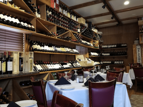 A cozy restaurant interior featuring wooden shelves lined with wine bottles and elegantly set tables.