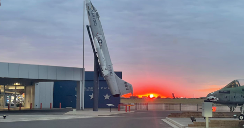 A missile display stands outside a military museum against a vibrant sunset sky.