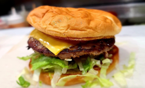 A close-up of a cheeseburger with a beef patty, melted cheese, and lettuce on a toasted bun.