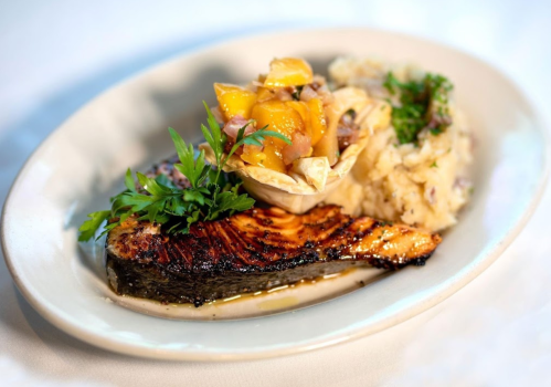 Grilled salmon fillet with a mango salsa, served with creamy rice and garnished with fresh herbs on a white plate.