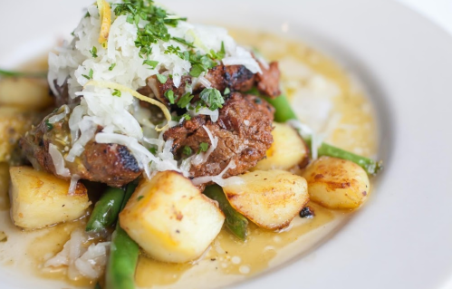 A plate of grilled meat topped with shredded cabbage, served with potatoes and green beans in a savory sauce.
