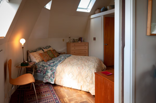 Cozy bedroom with a sloped ceiling, a bed with patterned bedding, a wooden dresser, and a warm light fixture.
