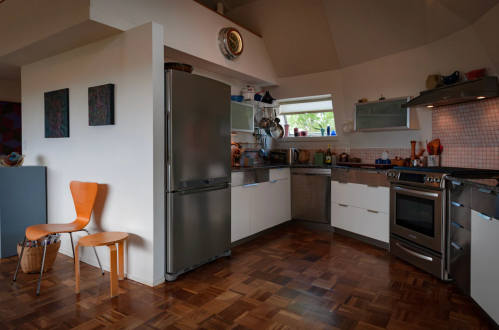 Modern kitchen with stainless steel appliances, wooden flooring, and a cozy seating area featuring a chair and basket.