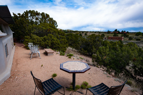 A scenic outdoor area with a table and chairs, surrounded by greenery and a view of distant hills under a cloudy sky.