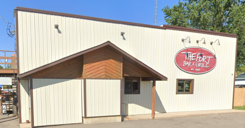 Exterior of The Fort Bar & Grill, featuring a wooden awning and a large sign, set against a clear blue sky.