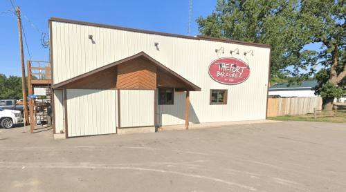 Exterior of a building labeled "The Fort Bar & Grill," featuring a wooden entrance and a clear blue sky.