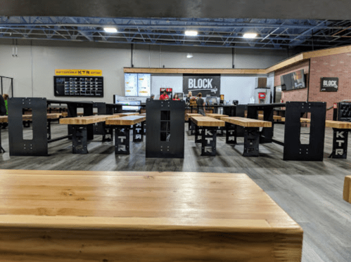 A spacious indoor area with multiple wooden tables and black metal frames, featuring a modern design and a casual atmosphere.