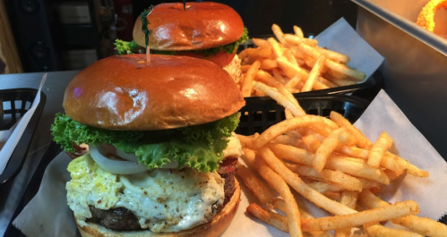 Two gourmet burgers with lettuce, tomato, and fried egg, served with a side of golden French fries.