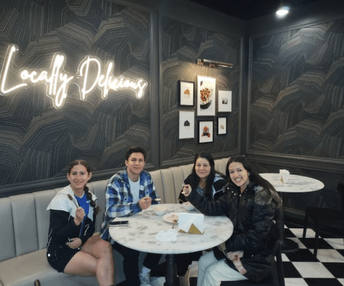Four people enjoying dessert at a stylish café with a "Locally Delicious" sign on the wall.