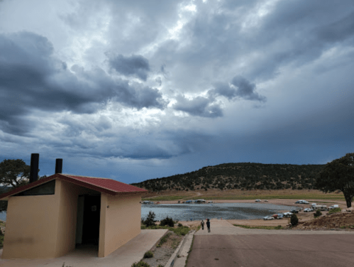 A cloudy sky over a lake with a small building and two people walking along a road.