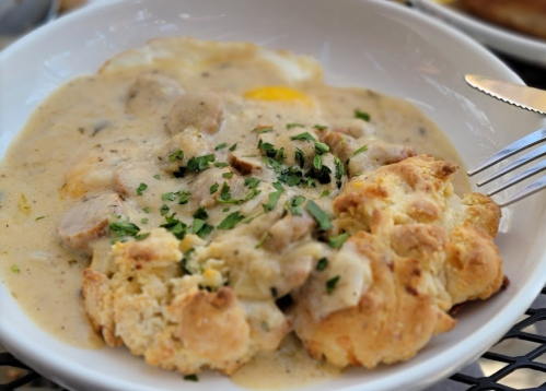 A bowl of biscuits smothered in creamy sausage gravy, garnished with chopped parsley.