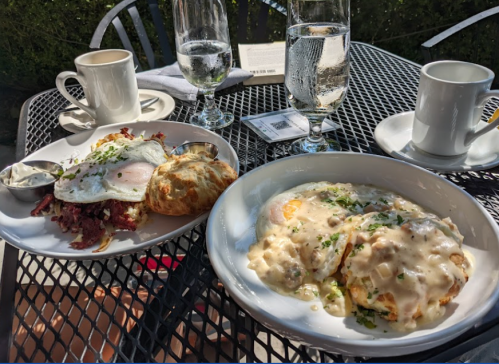 A table set with two plates: one with eggs, corned beef, and a biscuit; the other with biscuits and gravy.