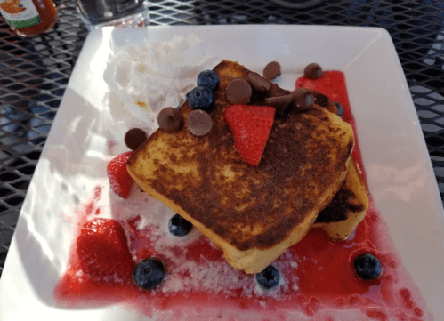 A plate of French toast topped with strawberries, blueberries, chocolate chips, and whipped cream on a berry sauce.