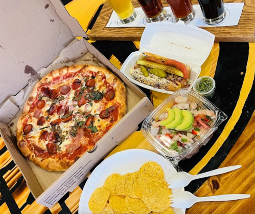 A pizza with pepperoni and herbs, a container of tacos with toppings, shrimp with avocado, and a bowl of tortilla chips.