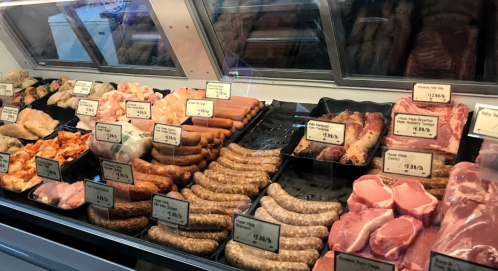 A display case filled with various meats, including sausages, chicken, and pork, all labeled with prices.