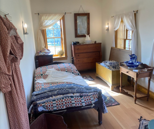 Cozy bedroom with a bed, wooden furniture, and decorative textiles, illuminated by natural light from a window.