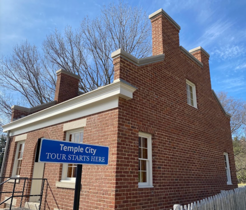 A brick building with a sign reading "Temple City Tour Starts Here" against a clear blue sky.