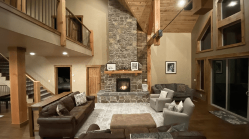 Cozy living room with a stone fireplace, wooden beams, and comfortable seating, illuminated by warm lighting.