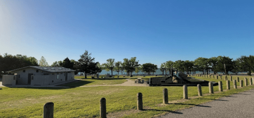 A serene park scene with a clear blue sky, grassy areas, trees, and a view of a lake in the background.