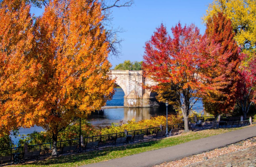 A scenic view of a bridge over a river, framed by vibrant autumn trees in shades of orange and red.