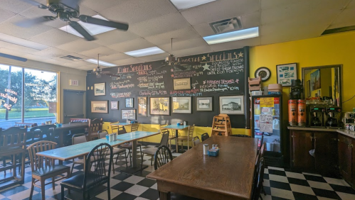 Cozy diner interior with yellow walls, checkered floor, chalkboard menu, and wooden tables and chairs.