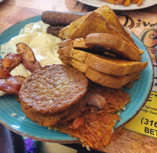 A plate of breakfast featuring toast, sausage, bacon, eggs, and a round meat patty on a bed of hash browns.