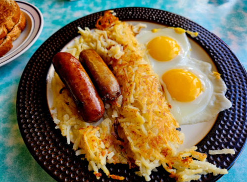 A plate with two fried eggs, crispy hash browns, and two sausages.