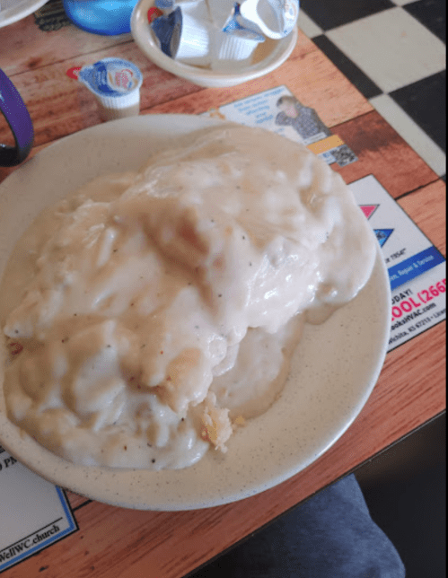 A plate of biscuits smothered in creamy sausage gravy, served on a casual dining table.