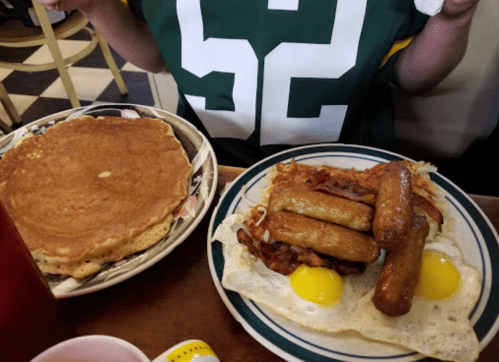 A plate of breakfast with pancakes, eggs, sausage, and hash browns, served on a table.