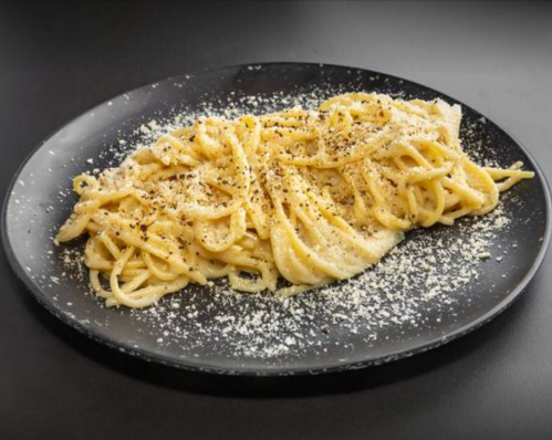 A plate of creamy pasta topped with grated cheese and black pepper on a dark background.