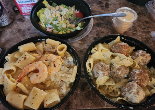 Two bowls of pasta: one with shrimp and creamy sauce, the other with meatballs, alongside a side salad.