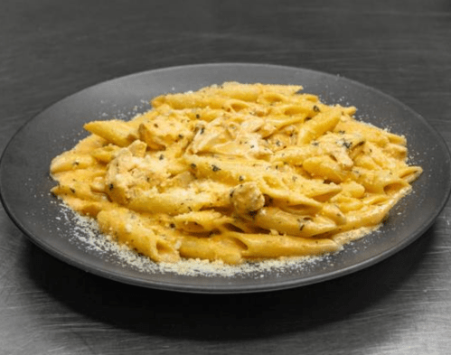 A black plate filled with creamy penne pasta topped with grated cheese and herbs.