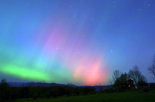 A vibrant aurora borealis lights up the night sky with shades of green, pink, and purple over a serene landscape.