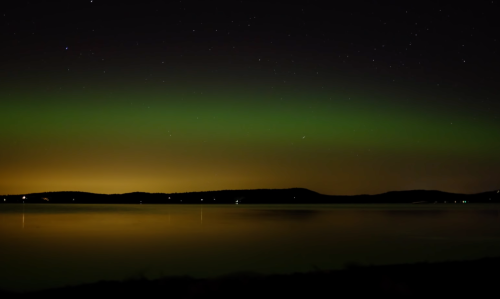 A serene night scene featuring a calm lake reflecting green auroras and a starry sky above.