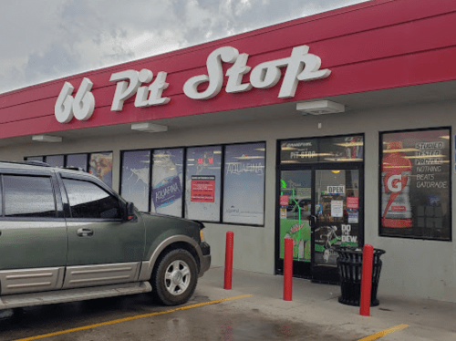 A green SUV parked outside a convenience store with a red and white "66 Pit Stop" sign and large windows.