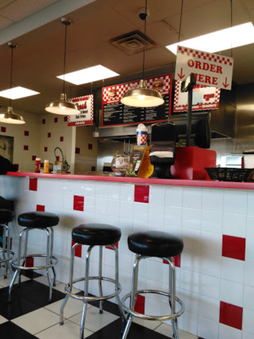A diner counter with red and white decor, stools, and a menu board displaying "Order Here" signs.