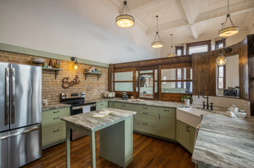 A modern kitchen with green cabinets, stainless steel appliances, and a rustic wooden accent wall. Bright and spacious design.