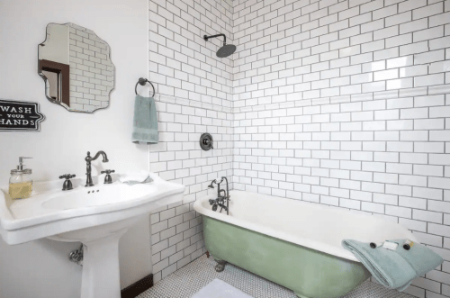 A stylish bathroom featuring a vintage green bathtub, white subway tiles, and a pedestal sink with a mirror.