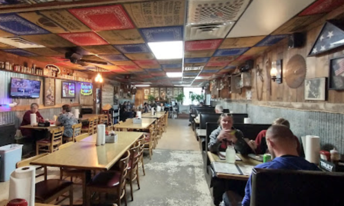 Interior of a rustic restaurant with wooden decor, tables, and patrons dining. Walls feature various memorabilia.