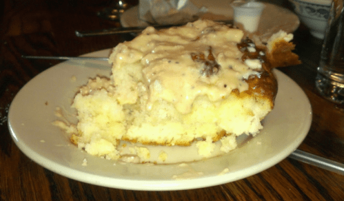 A slice of cake topped with creamy frosting on a white plate, with a fork resting beside it.