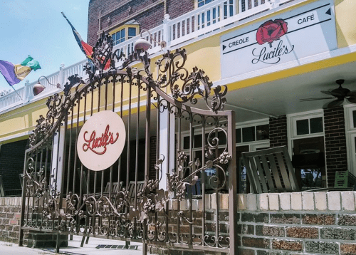 Wrought iron gate with "Lucile's" sign, leading to a colorful café with a Creole theme. Flags are visible above.