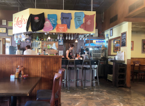 Interior of a restaurant bar with staff working, featuring hanging shirts and a cozy dining area.