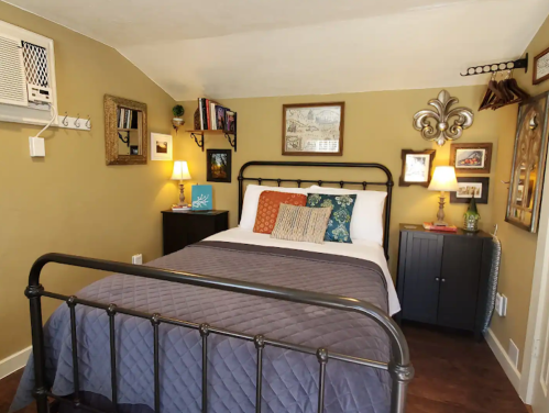 Cozy bedroom with a metal bed frame, decorative pillows, wall art, and a small nightstand in warm tones.
