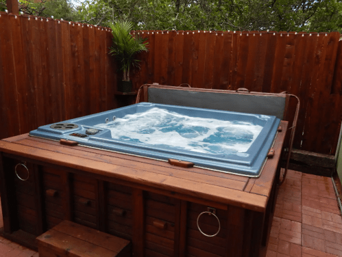 A wooden hot tub with bubbling water, surrounded by a wooden fence and potted plants.