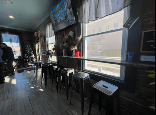 A cozy interior with a long bar, stools, and a window, featuring decorations and a TV in a warm atmosphere.