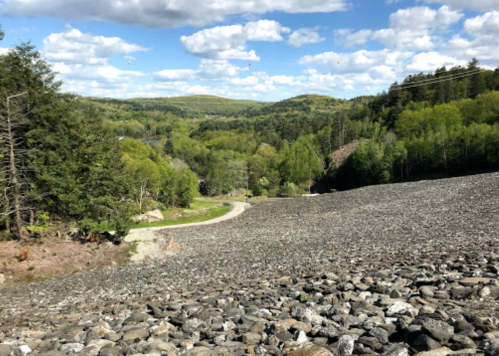 A rocky landscape with a winding path, surrounded by lush green trees and a blue sky with fluffy clouds.